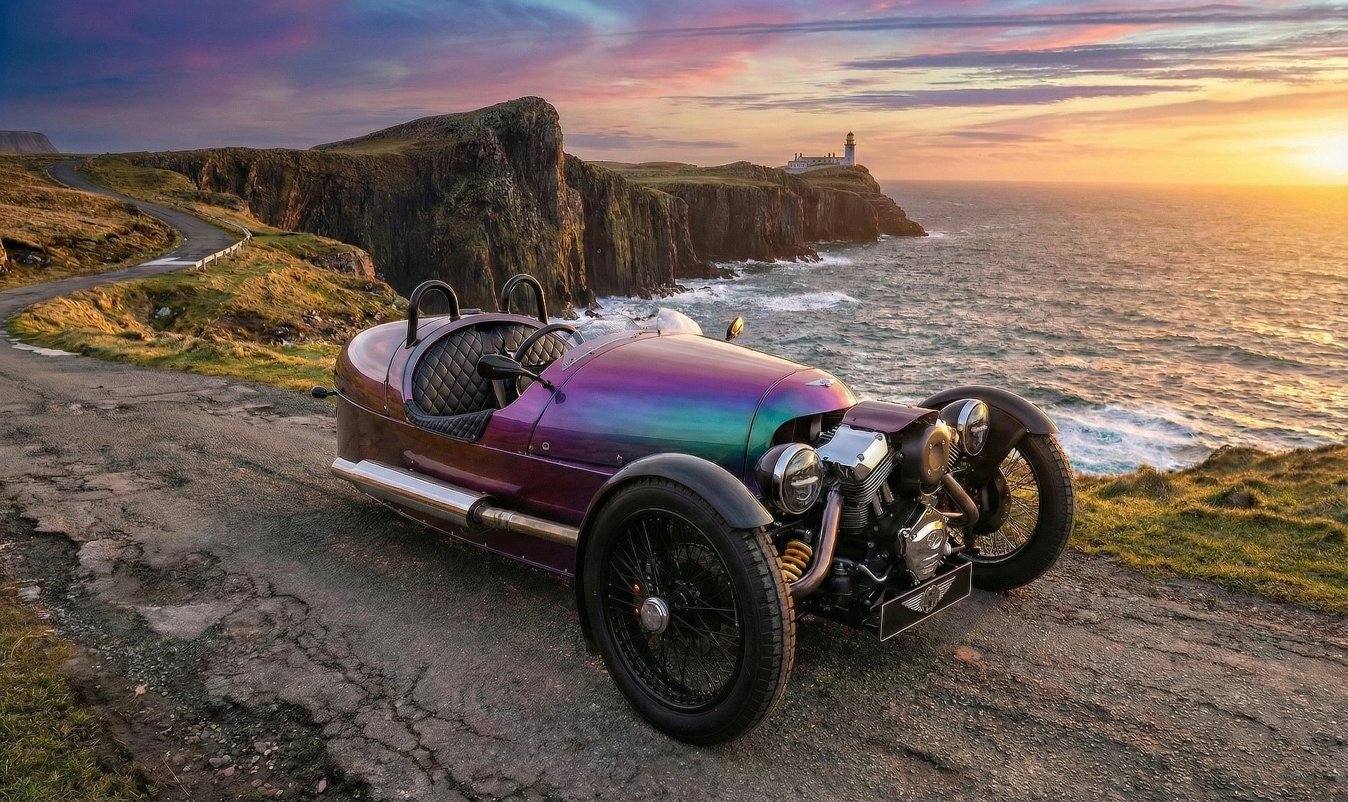 Iridescent purple Morgan 3 Wheeler parked on a coastal cliff road at sunset, near a lighthouse