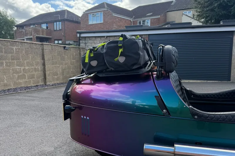 A Morgan 3 Wheeler with luggage strapped to the rack, seen from the side